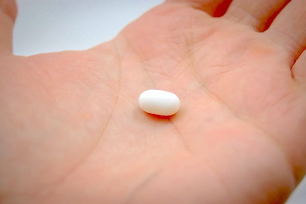 A white pill being held in the palm of a hand.